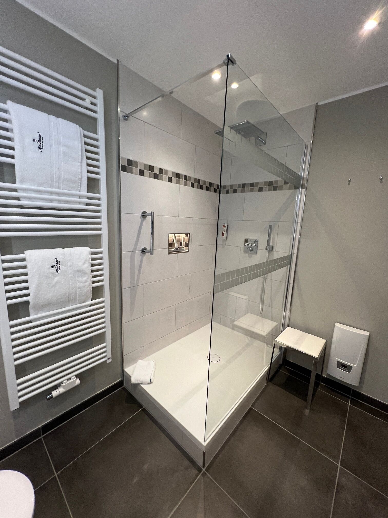 A modern bathroom with a glass-enclosed shower, a white sink, and a towel rack with multiple towels.