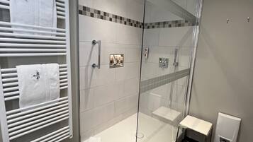 A modern bathroom with a glass-enclosed shower, a white sink, and a towel rack with multiple towels.