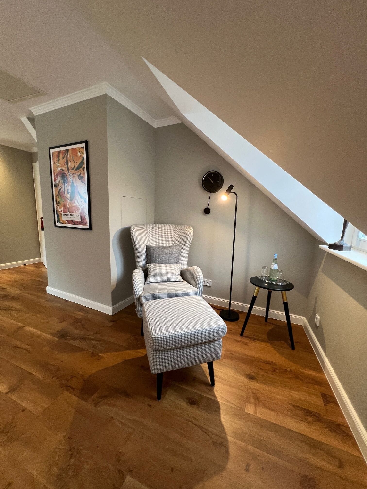 Un dormitorio estilo loft acogedor con un reposapiés de cuadros, una silla, una lámpara de pie y un cuadro en la pared.