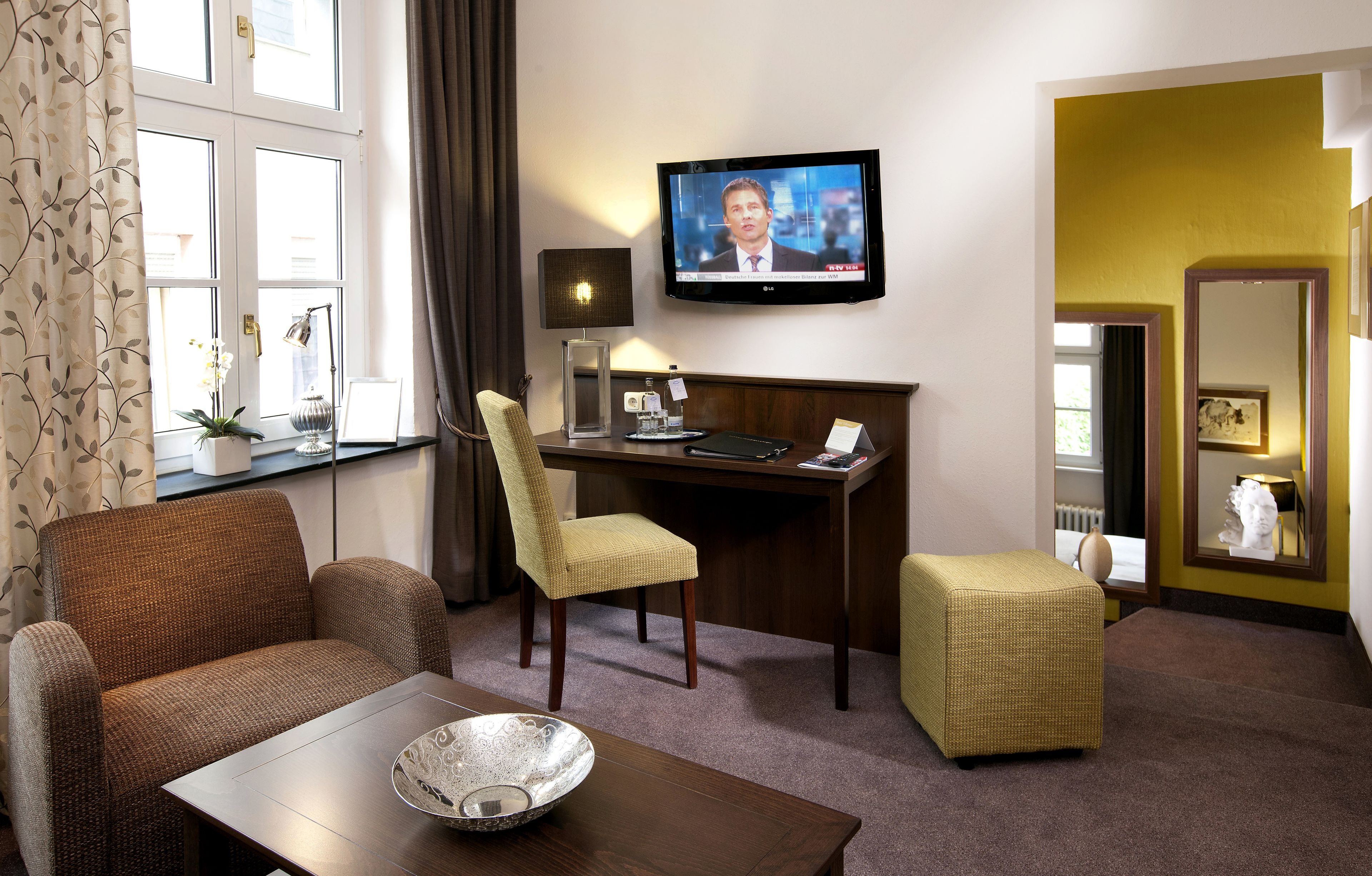 A hotel room with a television, a desk, a chair, a sofa, and a small table.