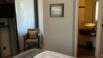 A hotel room with a bed, a chair, a television, a framed picture on the wall, and a bathroom visible through an open door.