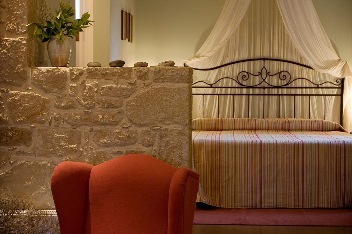 A bedroom with a stone wall, a bed with a canopy, and a red armchair.