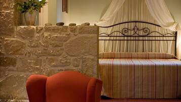A bedroom with a stone wall, a bed with a canopy, and a red armchair.