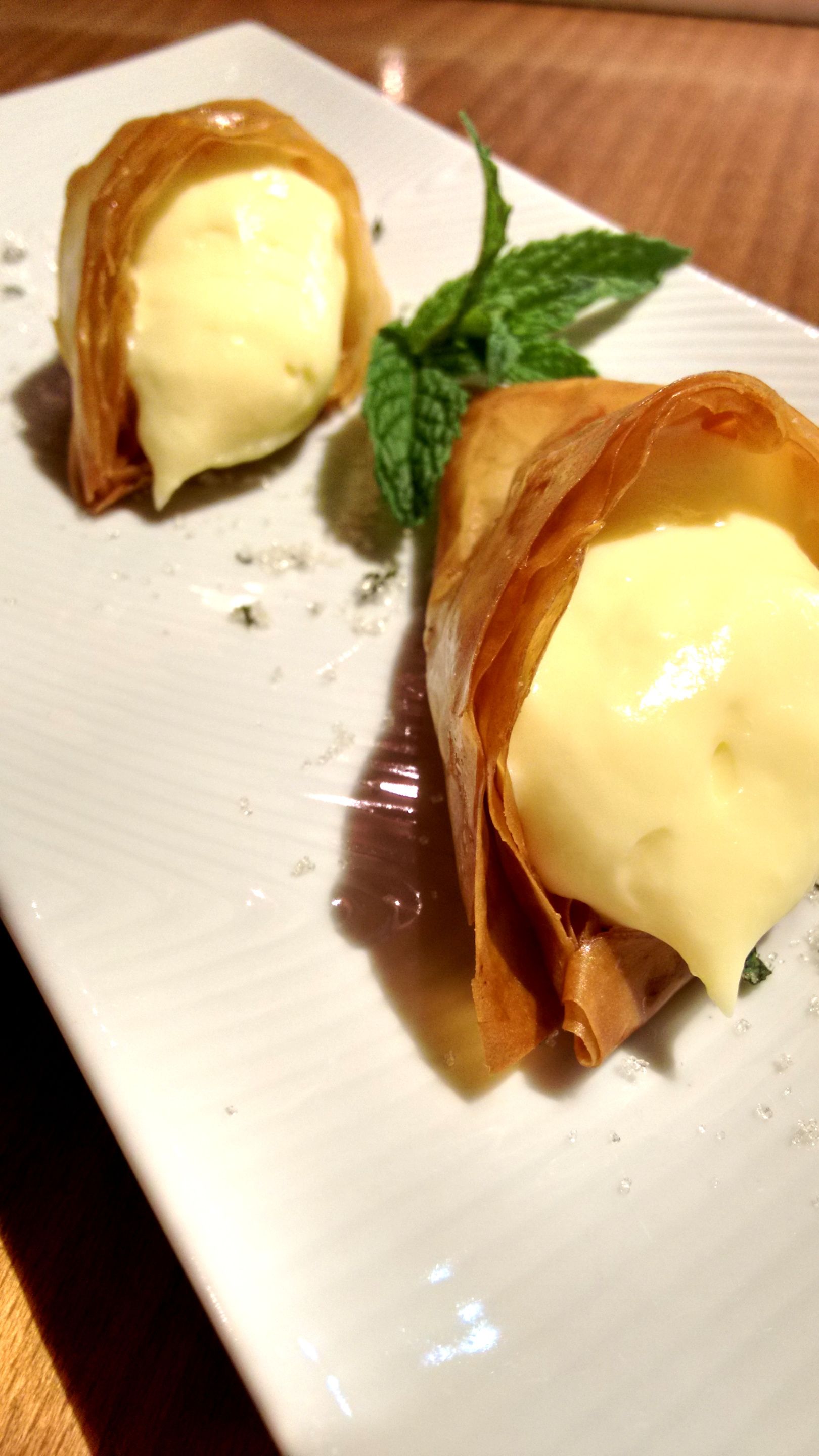 A plate with two pastries, one cut in half, and a mint leaf on a white plate.