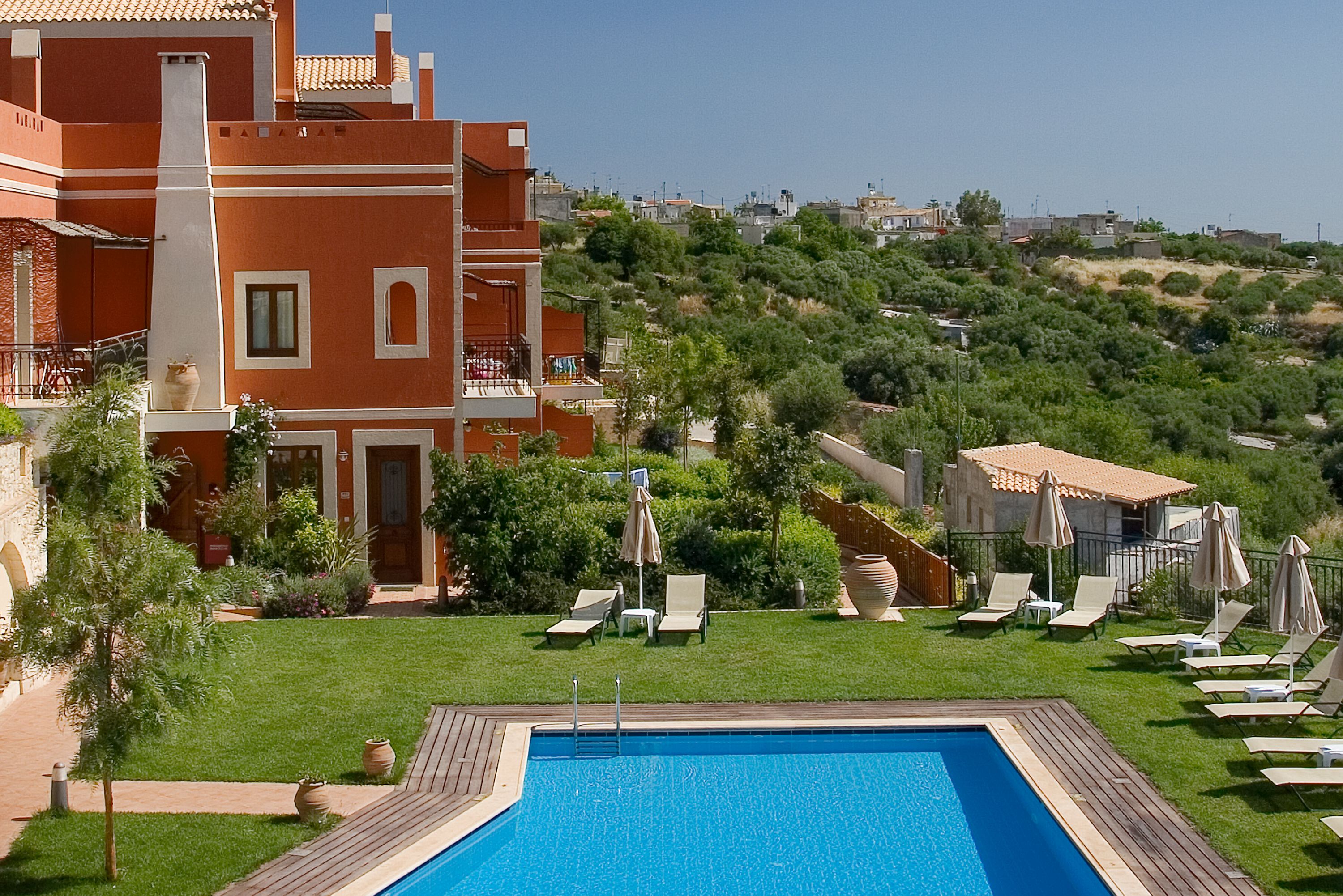 A hotel with a swimming pool, lounge chairs, and a view of a hilly landscape.