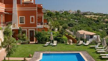 A hotel with a swimming pool, lounge chairs, and a view of a hilly landscape.