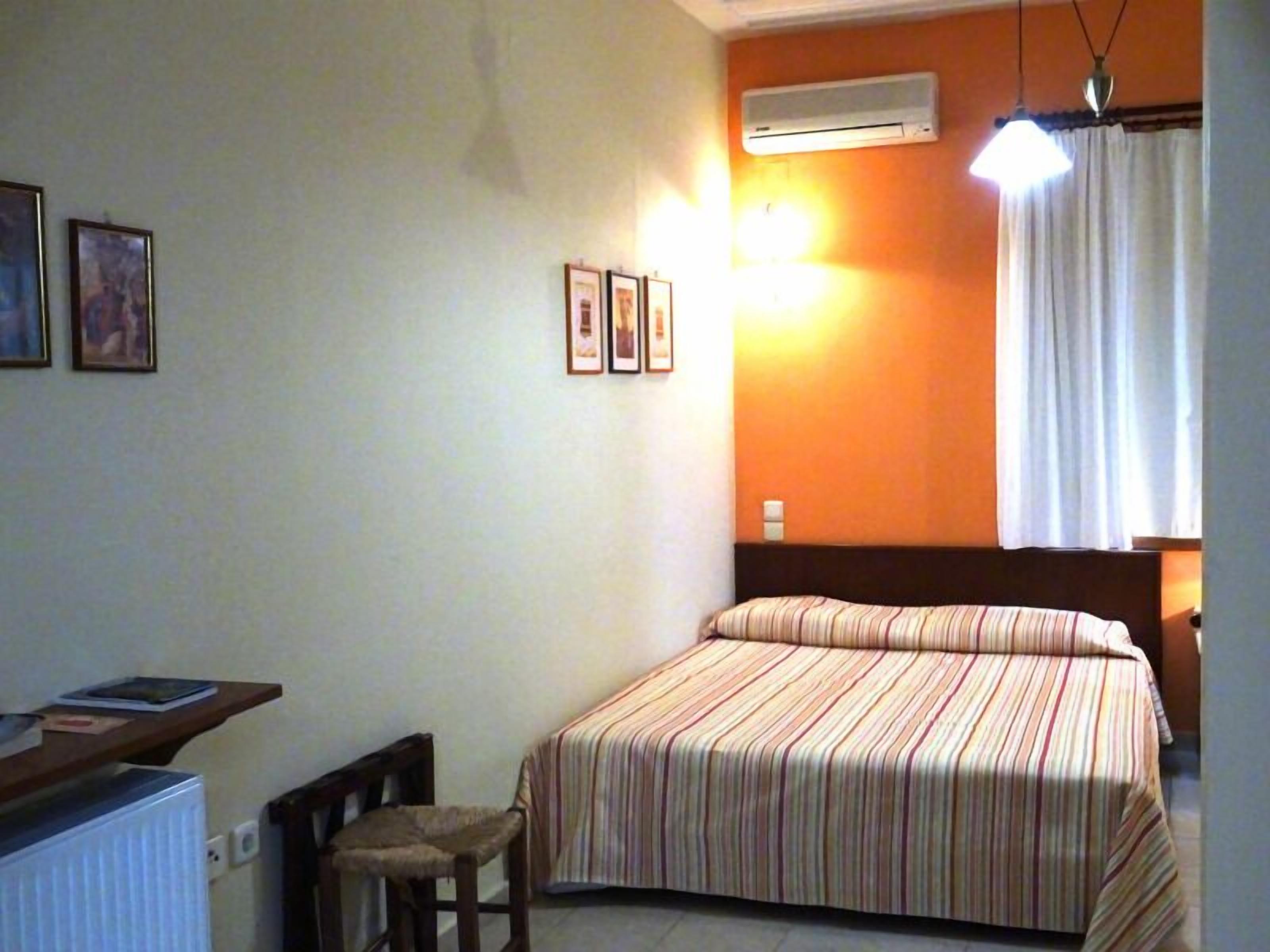 A bedroom with a bed, a chair, a desk, and an air conditioning unit.
