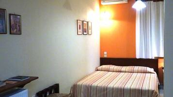 A bedroom with a bed, a chair, a desk, and an air conditioning unit.