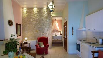 Una sala de estar acogedora con una pared de piedra, un sillón rojo, una mesa de comedor con fruta y una cocina con armarios blancos.