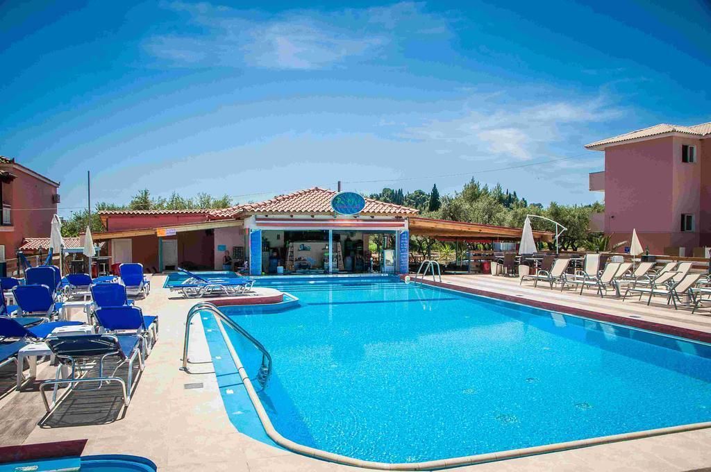 A swimming pool with lounge chairs and umbrellas, surrounded by buildings with a tiled roof.
