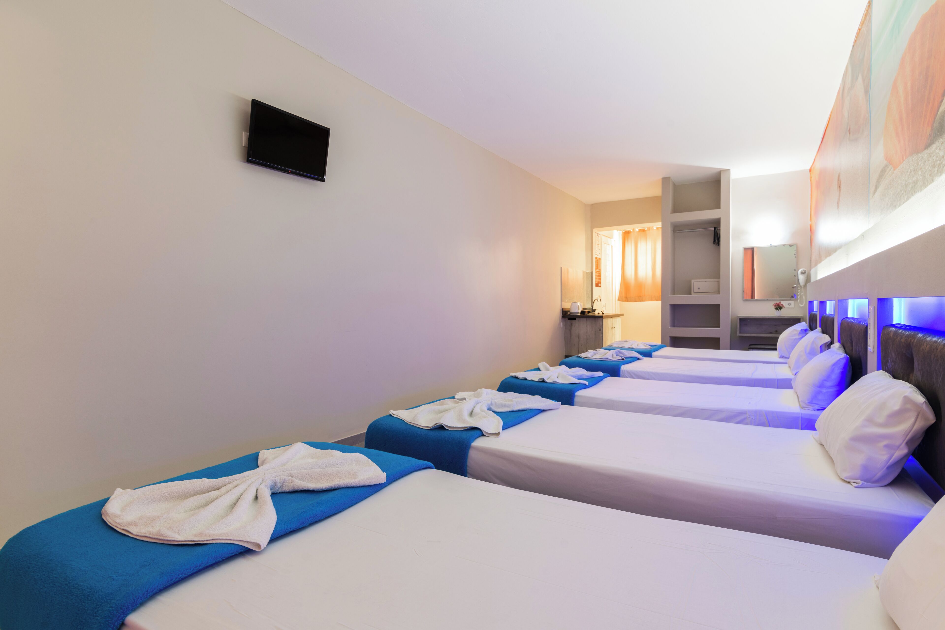 Een hotelkamer met vier eenpersoonsbedden, elk met een blauwe sprei en witte kussens, en een flatscreen televisie aan de muur.