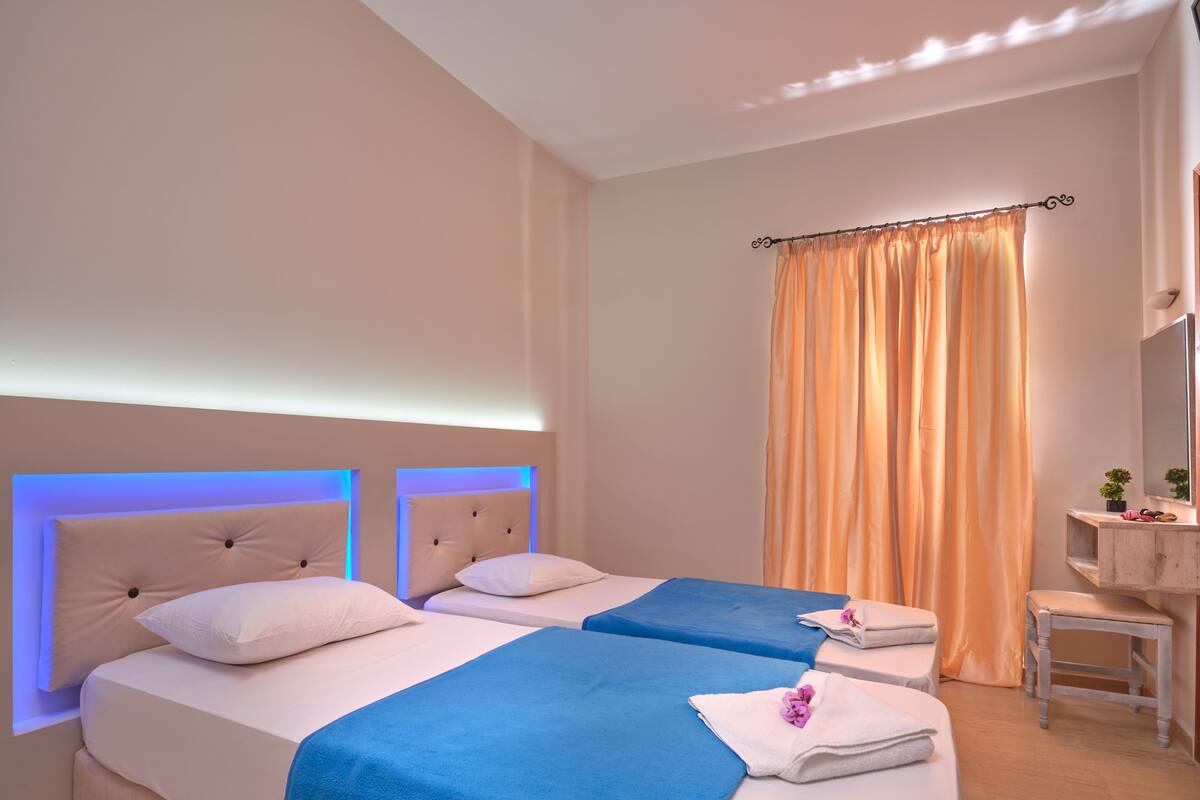 A hotel room with two beds, a small desk, a mirror, and a window with curtains.