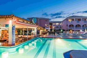 A hotel pool area with a bar, lounge chairs, and a building with balconies. - Savvas De Mar Hotel (Zakynthos)