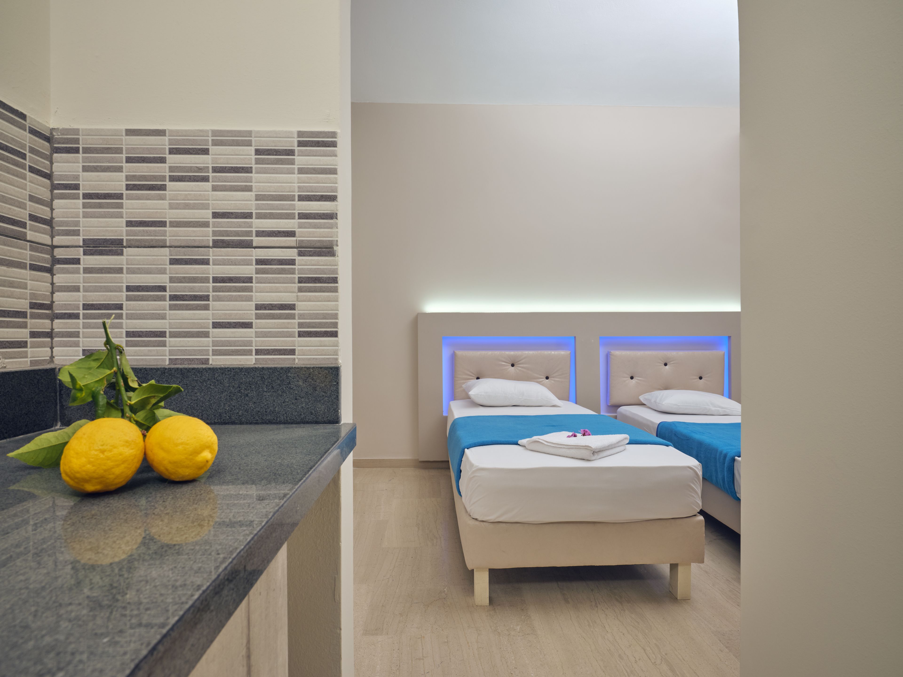 A hotel room with two beds, a small kitchenette, and a tiled backsplash.