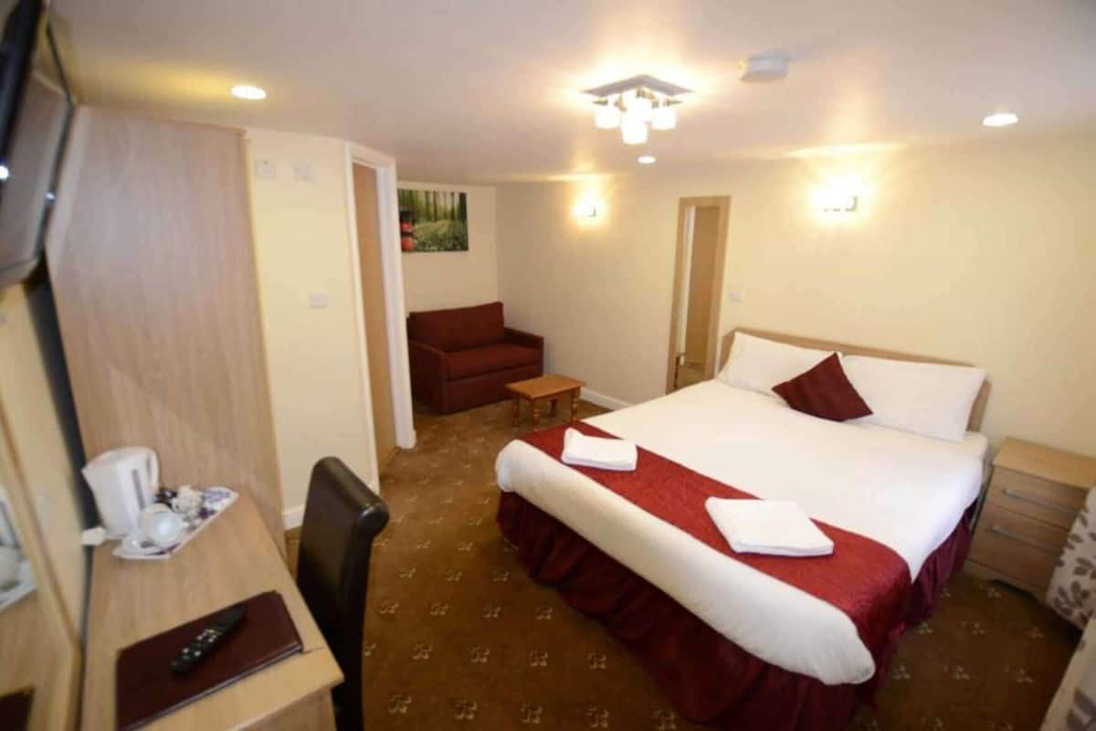 A hotel room with a bed, a desk with a chair, a red sofa, and a small table.