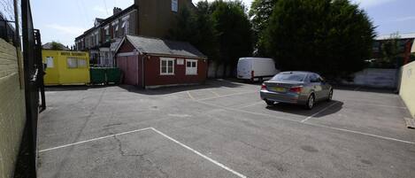 A parking area with a yellow security office, a red building, and a car.