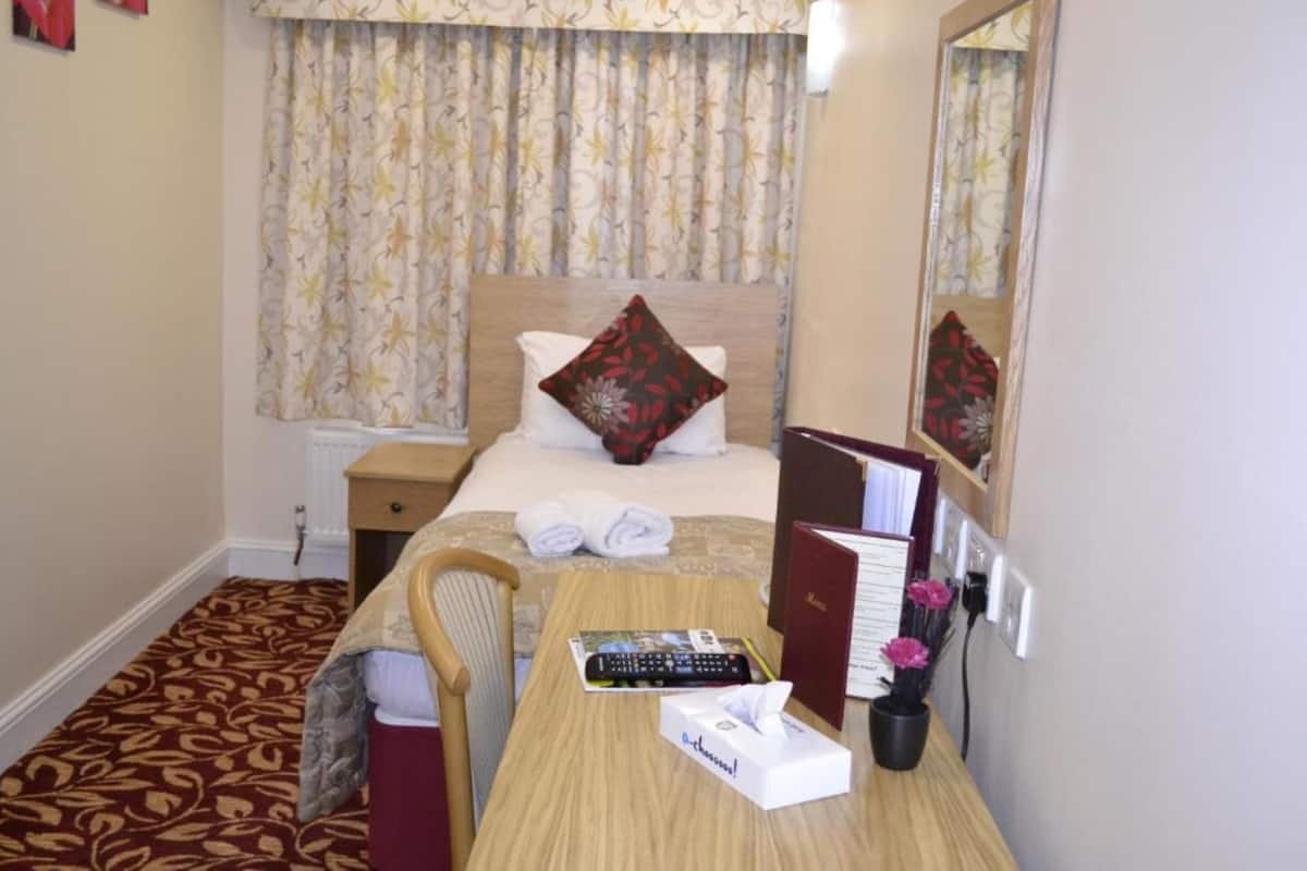 Habitación de hotel con cama, escritorio, silla, espejo y ventana con cortinas.