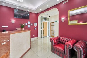Un espace d’accueil avec un comptoir en marbre, un canapé en cuir rouge et un miroir au mur.