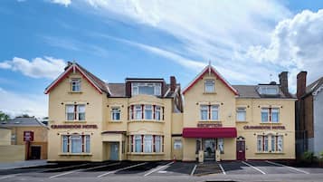 Un edificio de dos pisos con techo plano y toldo rojo, con la inscripción 'CRANBROOK HOTEL' y 'RECEPCIÓN'.
