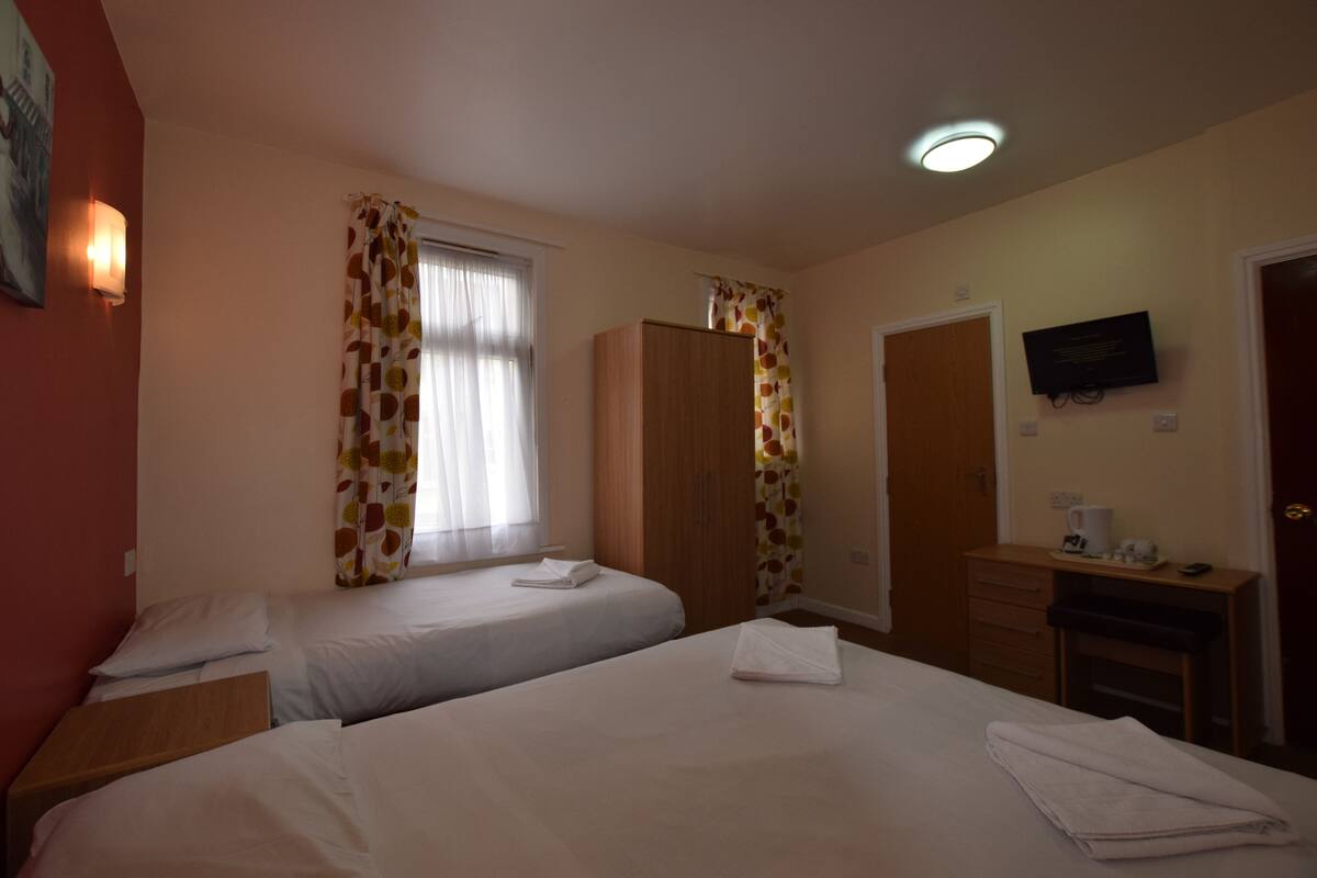 Habitación de hotel con dos camas, un armario de madera, un escritorio con televisor y una ventana con cortinas.