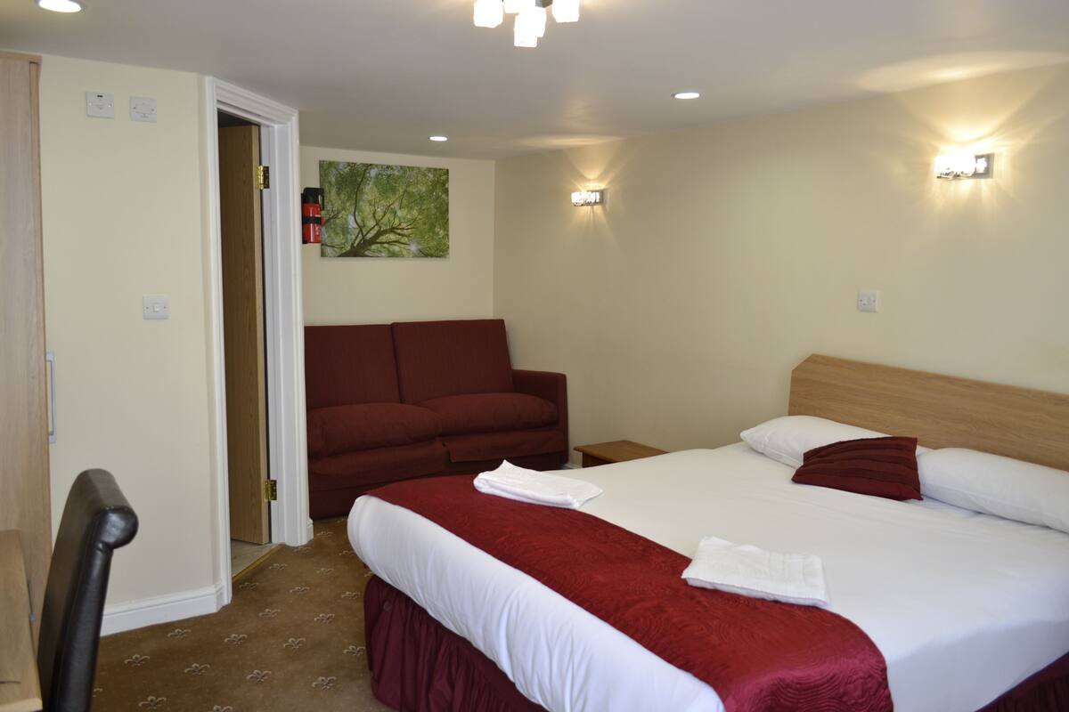 Habitación de hotel con una cama, cabecera de madera, sofá rojo y un cuadro en la pared.