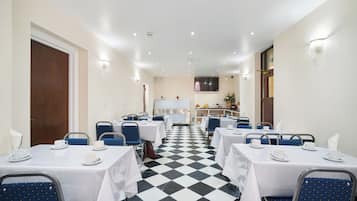 Un comedor de hotel con mesas y sillas, suelo a cuadros y una cocina al fondo.
