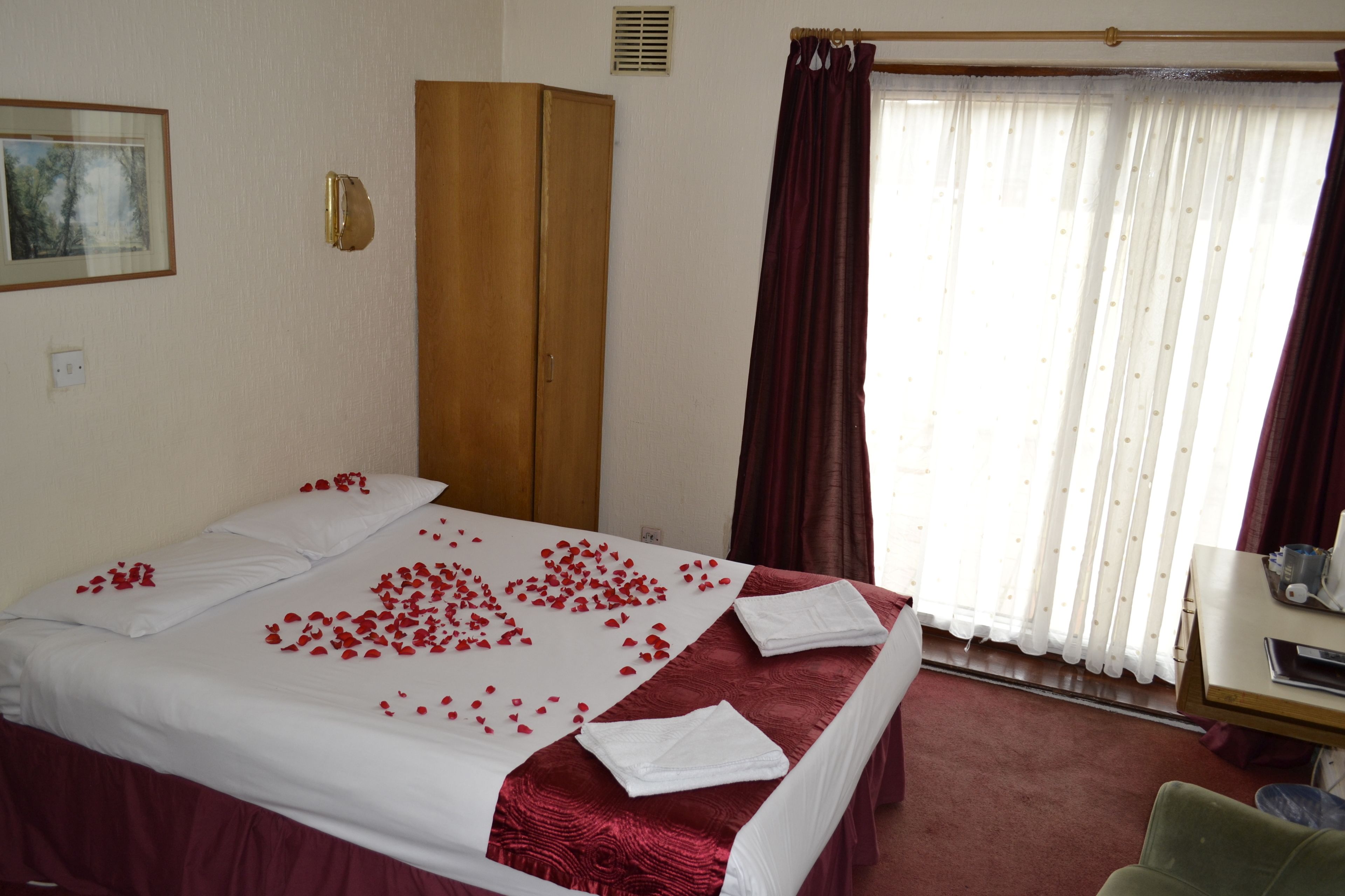 A hotel room with a bed, a wardrobe, a desk, and a window with curtains.