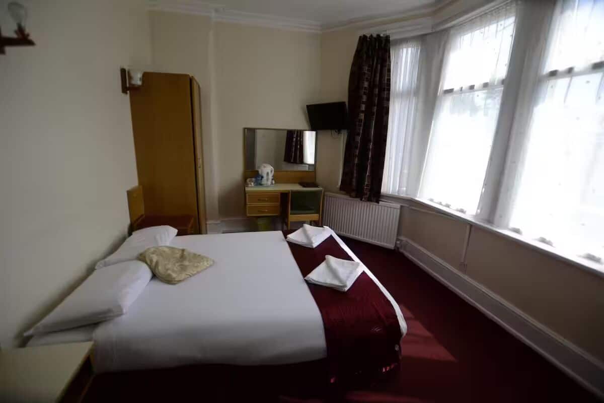 Una habitación de hotel con cama, cómoda, espejo, radiador y ventana con cortinas.