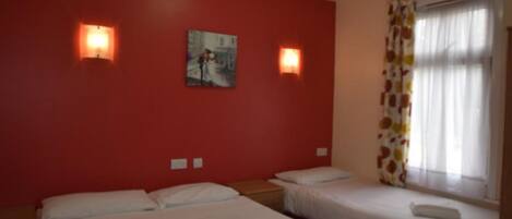 A hotel room with two beds, a red wall, and two wall-mounted lights.