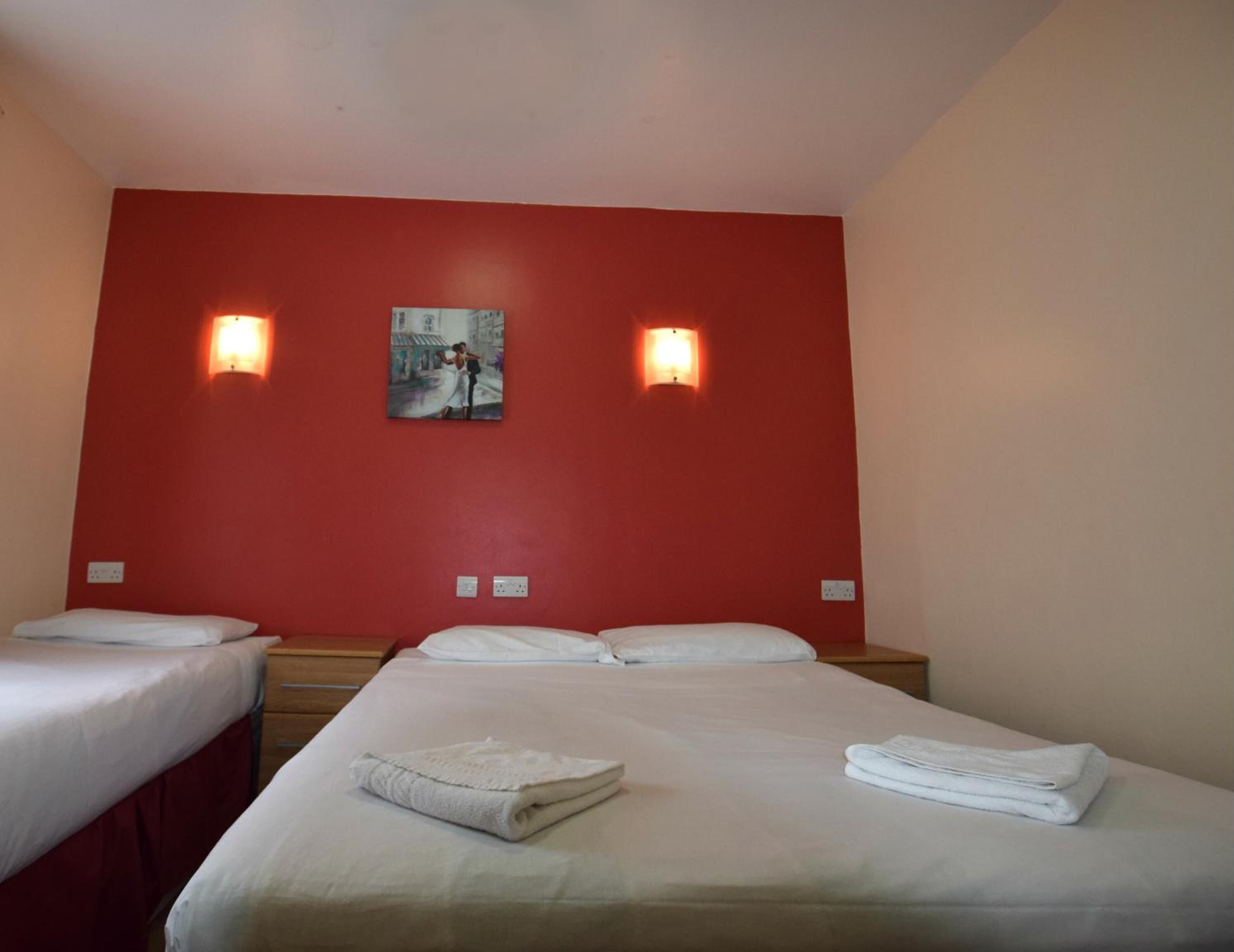 Habitación de hotel con dos camas individuales, una pared de acento roja y dos luces fijadas a la pared.