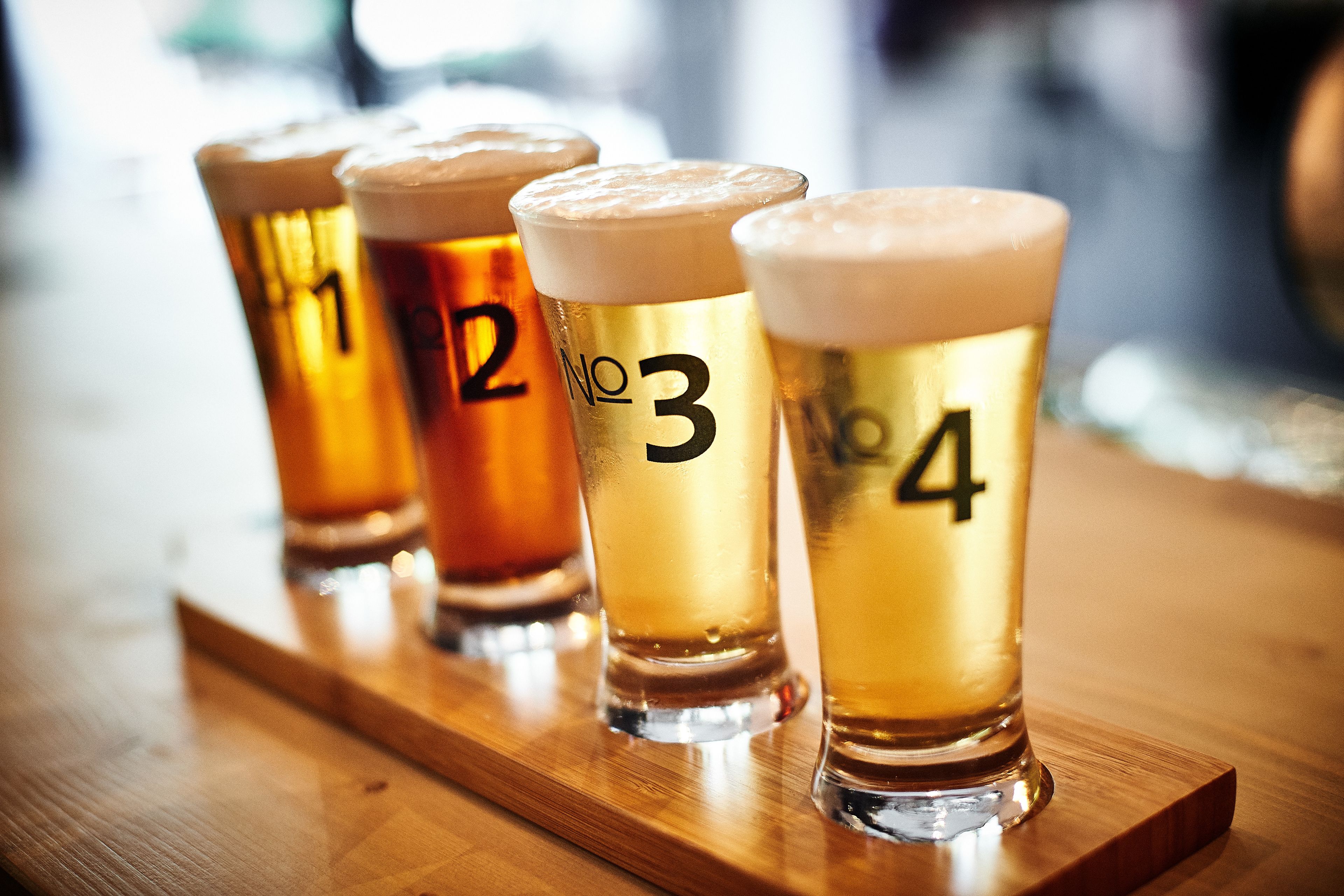 Four shot glasses of beer with numbers 1 to 4 on a wooden tray.