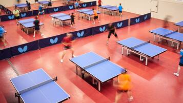 A table tennis facility with multiple tables and players in motion.