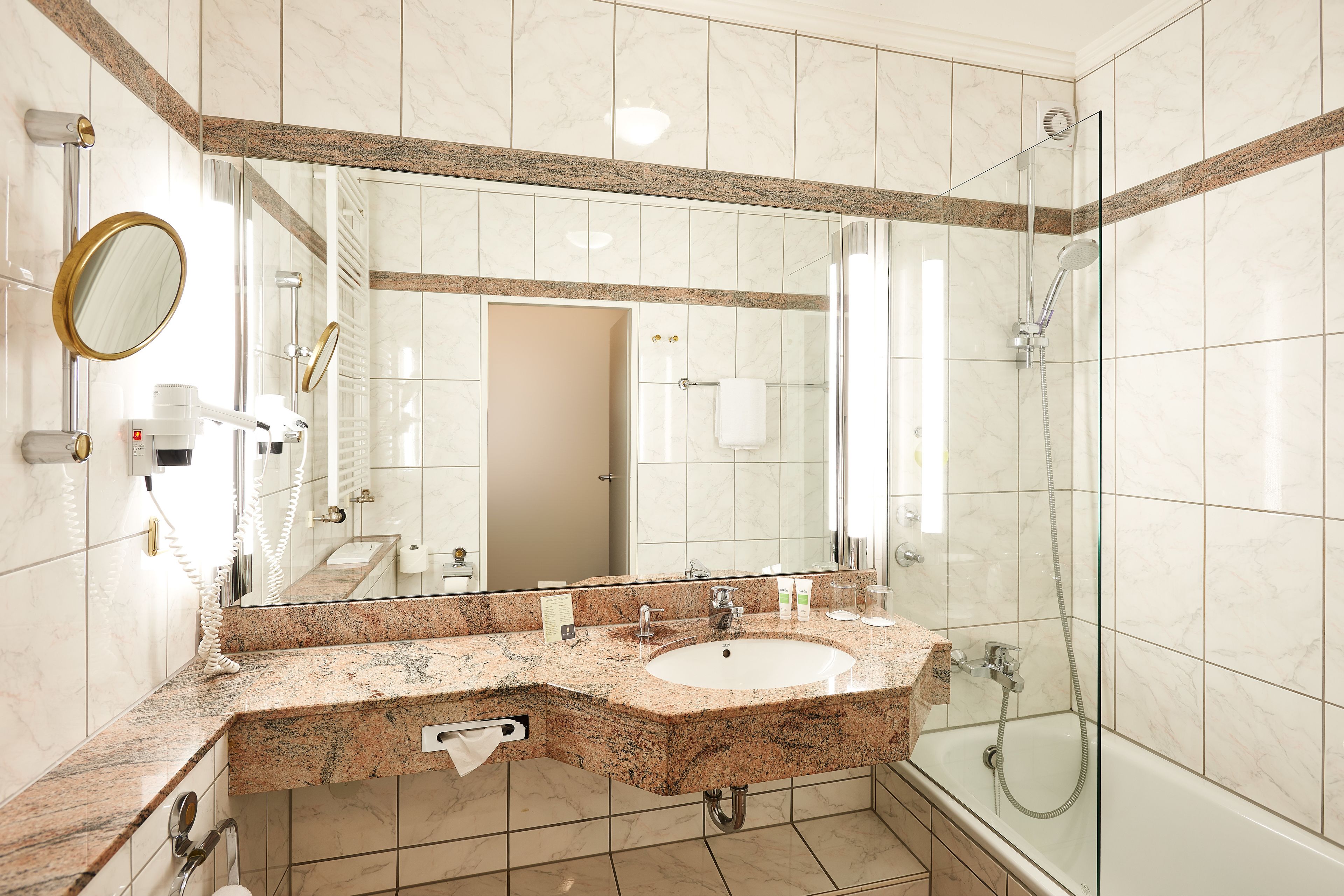 A modern bathroom with a granite countertop sink, a large mirror, and a glass-enclosed shower.