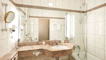 A modern bathroom with a granite countertop sink, a large mirror, and a glass-enclosed shower.