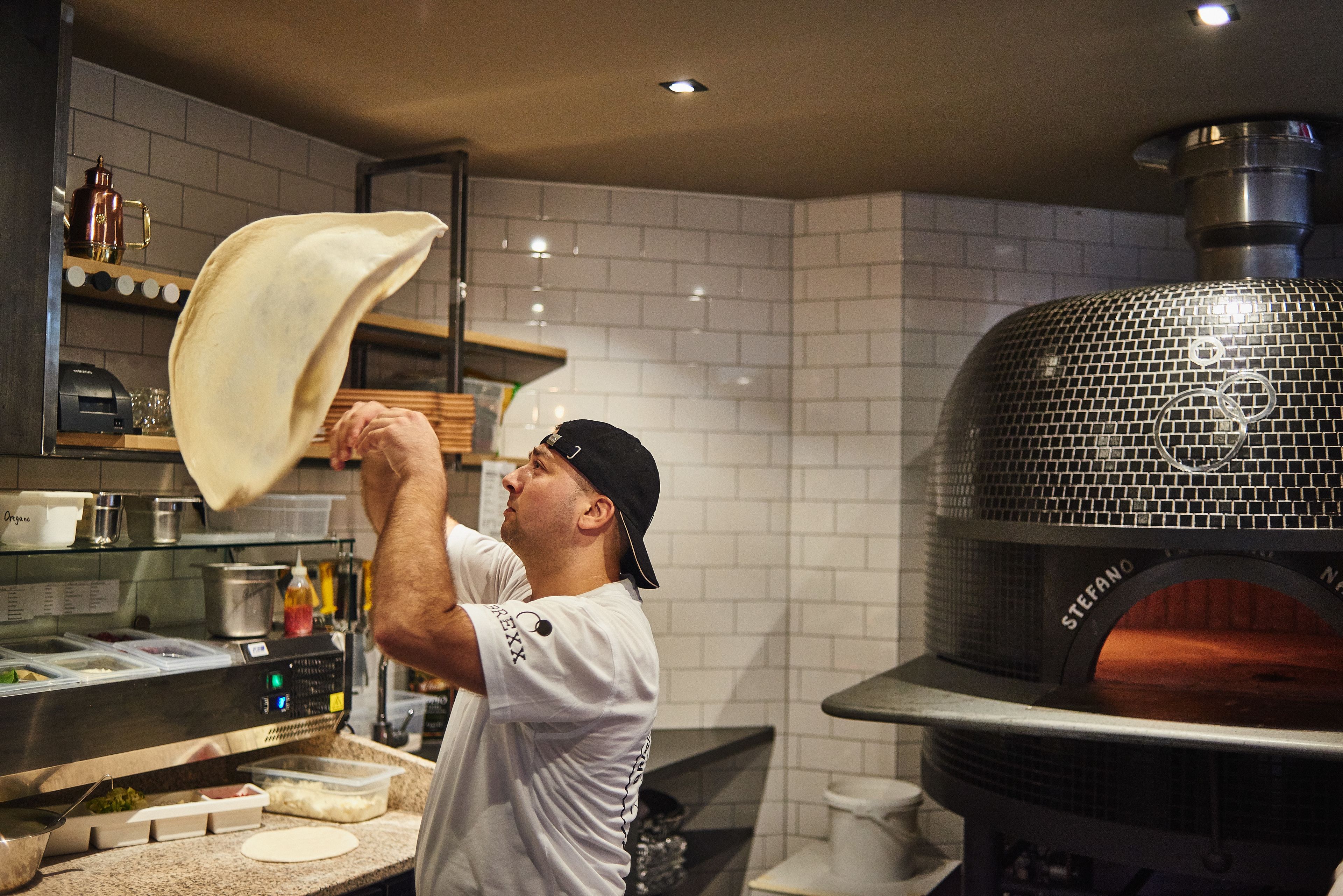 A chef preparing food in a kitchen with a large brick oven.
