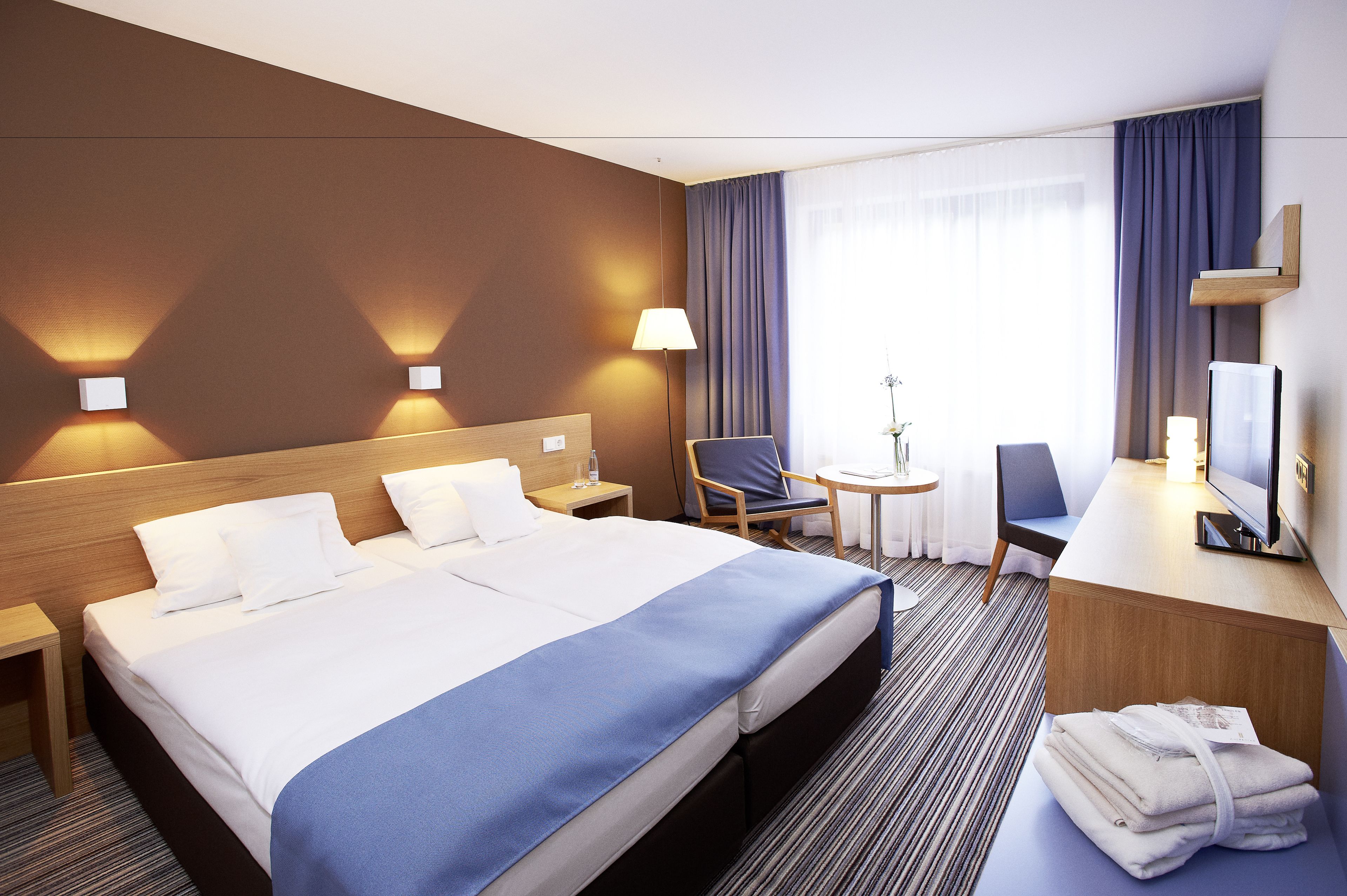 A hotel room with a large bed, a desk, a chair, and a TV.