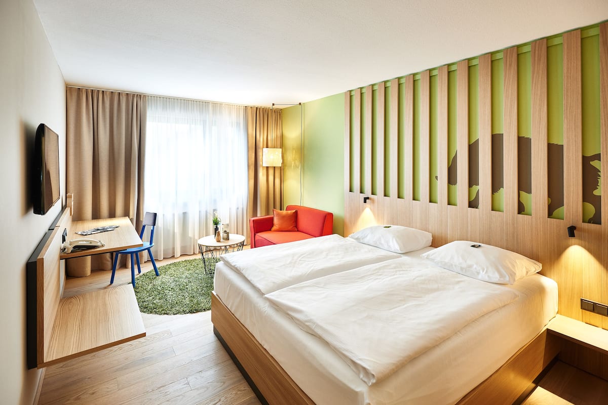 A hotel room with a bed, a desk, a chair, a small table, and a sofa.