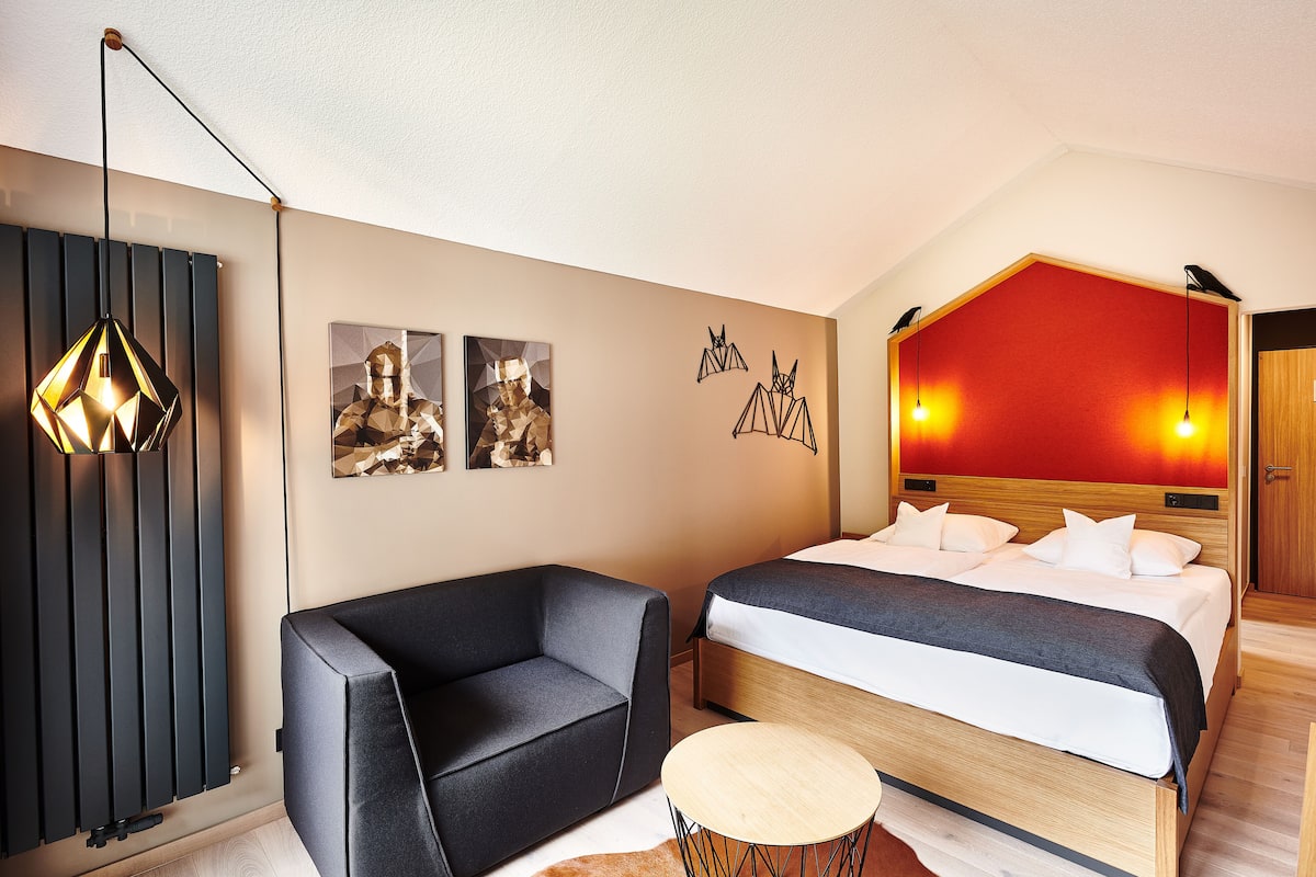 A modern hotel room with a bed, a sofa, a small round table, and a unique pendant light.