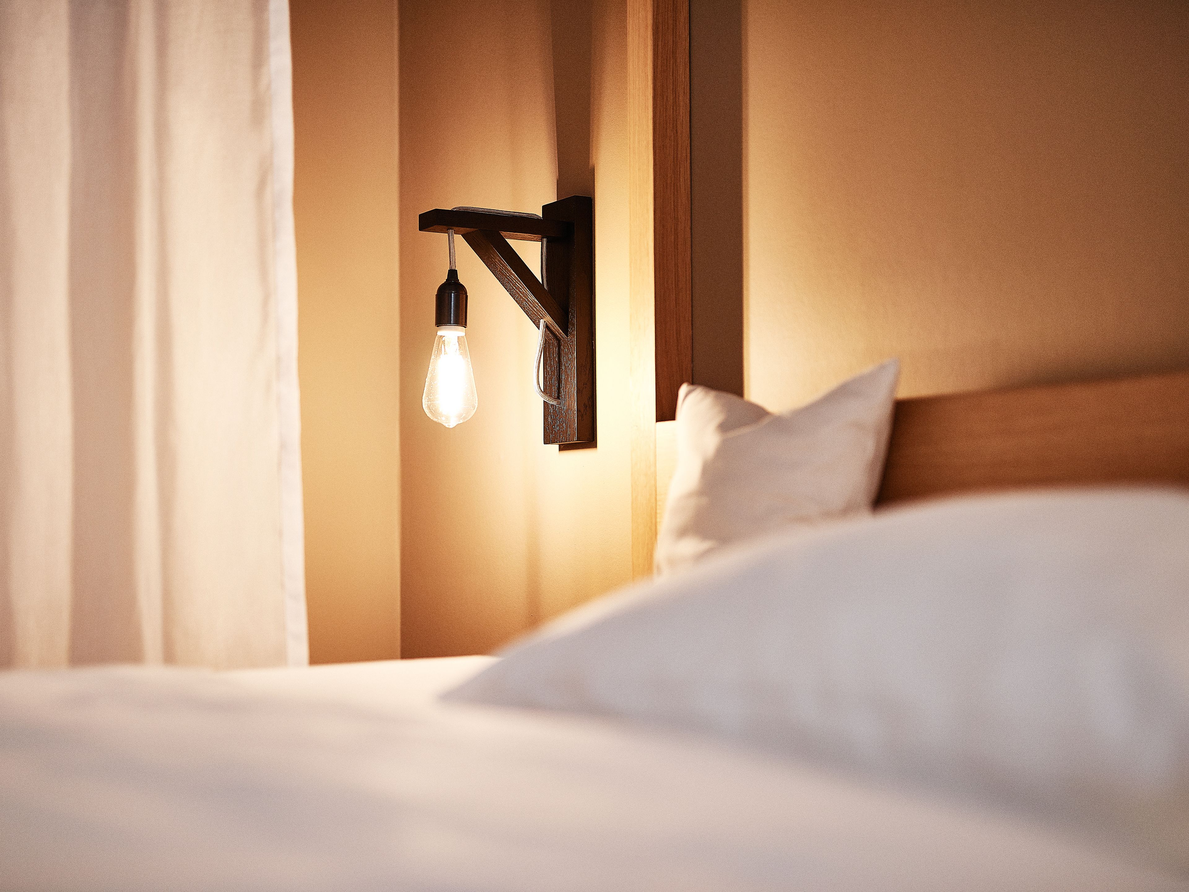 A hotel room with a bed, a wall-mounted light fixture, and a wooden headboard.