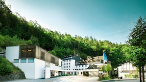A modern hotel with a courtyard, surrounded by lush greenery and a forested hillside. - Hotel Zugbruecke Grenzau (Hoehr-Grenzhausen)