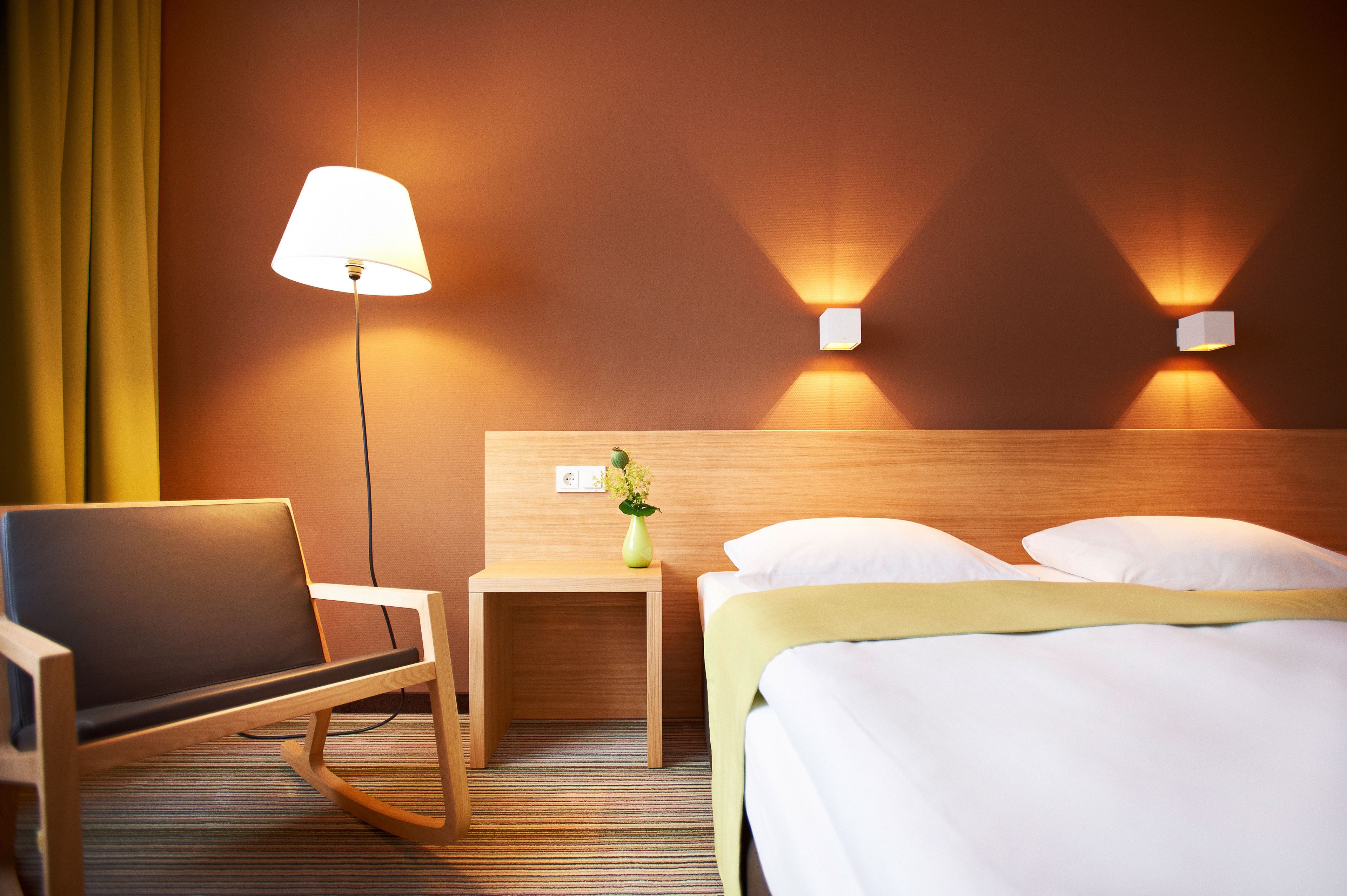 Ein Hotelzimmer mit einem Bett, einem Sessel, einem Nachttisch mit Lampe und zwei Wandleuchten.