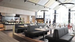 A modern restaurant with a bar area, seating, and a kitchen in the background. - Hotel Zugbruecke Grenzau (Hoehr-Grenzhausen)