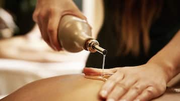 A close-up of a massage therapy session with a focus on the therapist's hands and the oil bottle.