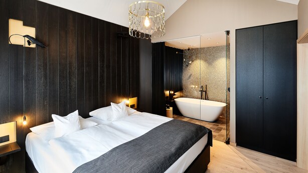 A modern bedroom with a large bed, bedside lamps, a bathtub, and a wardrobe. - Hotel Zugbruecke Grenzau (Hoehr-Grenzhausen)