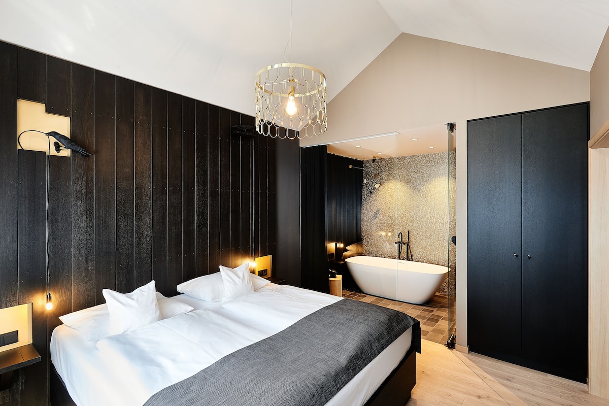 A modern bedroom with a large bed, bedside lamps, a bathtub, and a wardrobe.