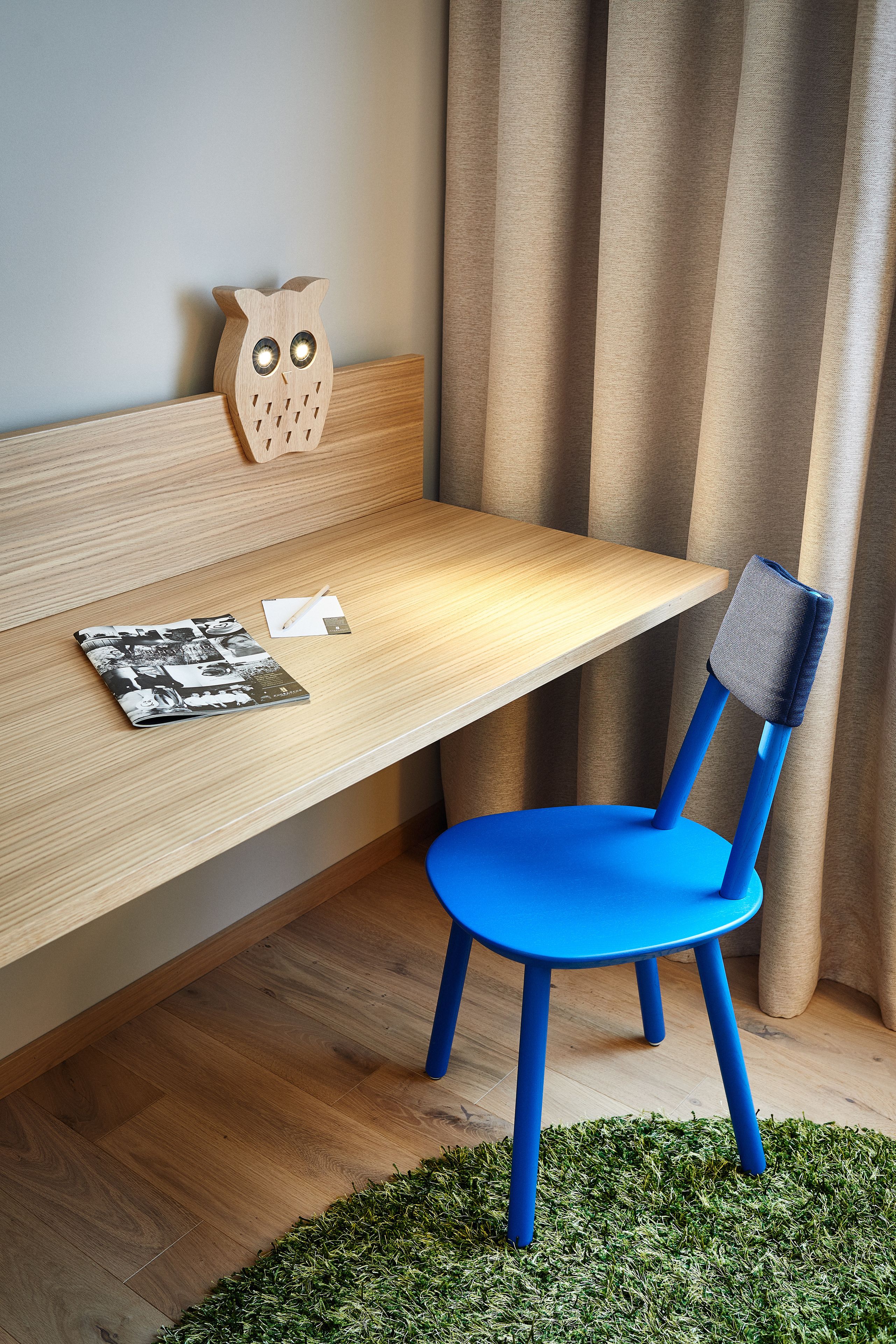 A wooden desk with a blue chair, a wooden owl decoration, and a magazine on the table.