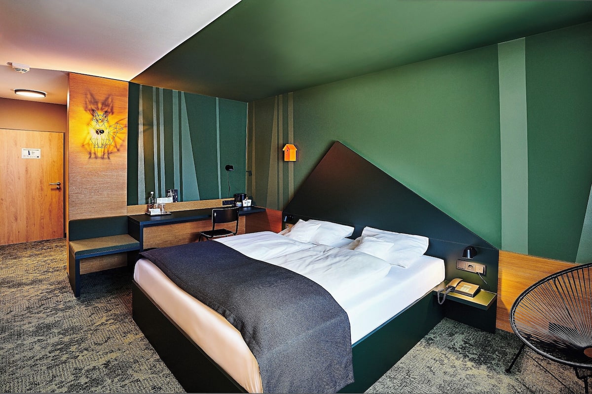 A hotel room with a bed, bedside table, chair, and a wall-mounted artwork.