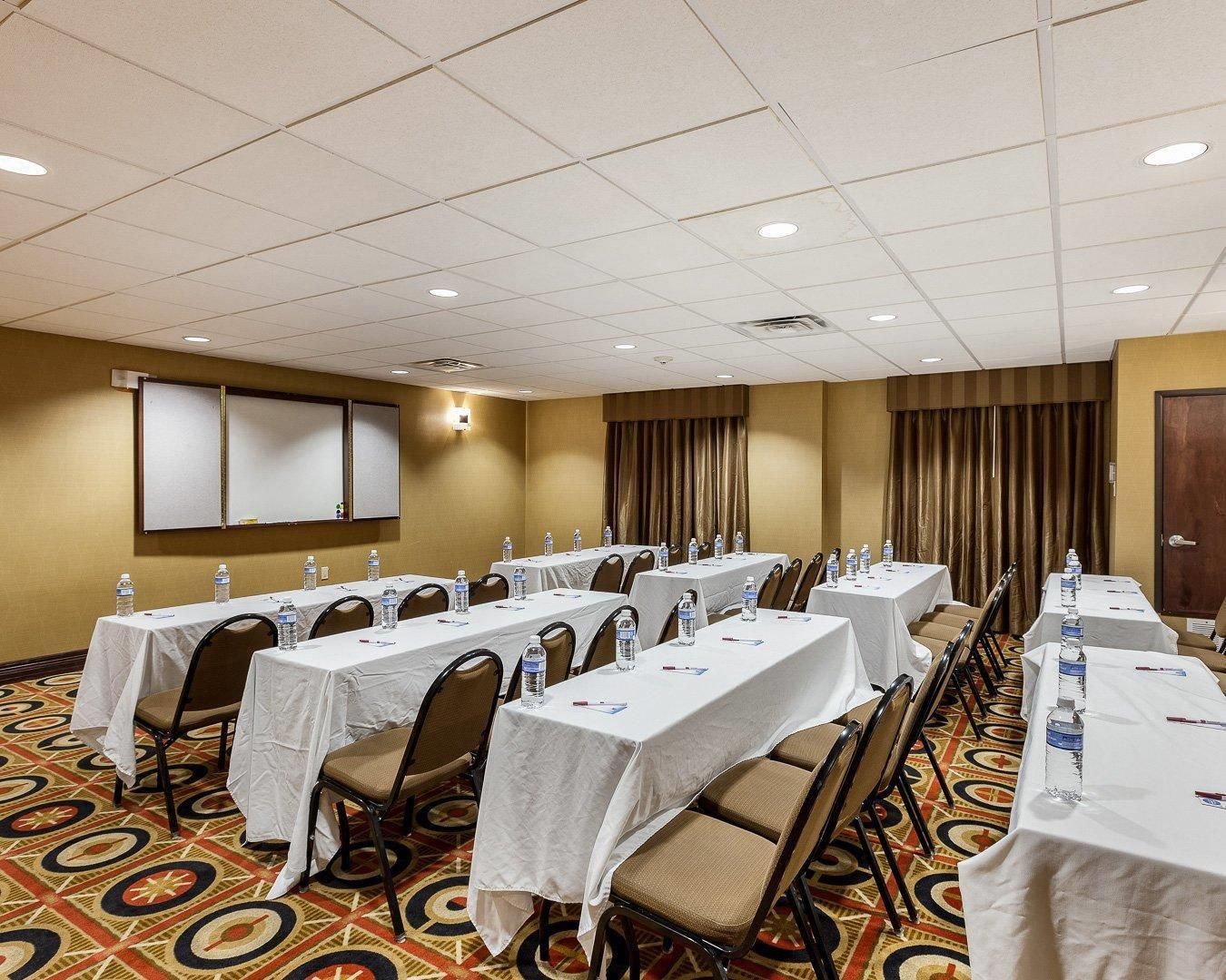 A conference room with tables set up for meetings, equipped with water bottles, and a projector screen on the wall.