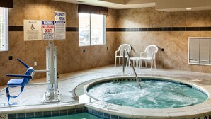 A spa area with a hot tub, two white chairs, a pool lift, and safety signs. - Comfort Suites Plano - Dallas North (Plano)