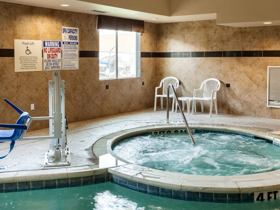 Uma área de spa com hidromassagem, duas cadeiras brancas, elevador para piscina e avisos de segurança.